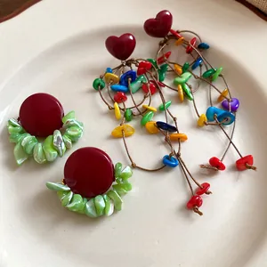 Detail view of red heart and round stud earrings with colorful shell tassel on a plate