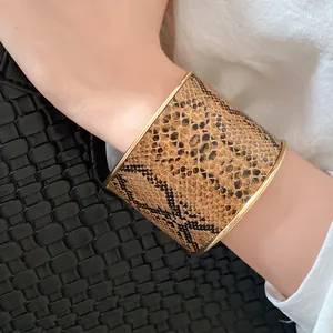 Detailed view of a wide gold-tone cuff bracelet with snakeskin leather inlay on wrist.