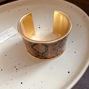 Detailed macro view of wide gold-tone cuff bracelet with luxury brown python pattern.