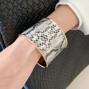 Close-up of wide snakeskin pattern cuff bracelet with gold metal edges on wrist