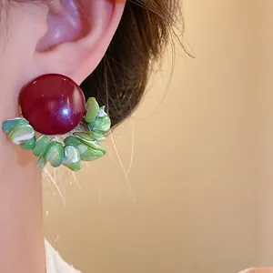 Close-up of vintage deep red stud earrings with polished green shell chip details
