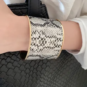 Detailed view of a wide cuff bracelet with snakeskin pattern and gold metal edges