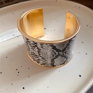 Detailed macro view of a gold-tone wide cuff bracelet with elegant snakeskin texture