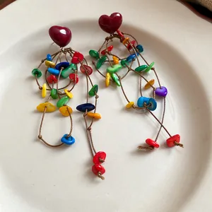 Detailed view of vintage heart earrings with colorful shell tassels on a ceramic plate.