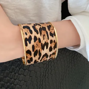 Detail view of a leopard print leather cuff bracelet with golden metal trim on a wrist