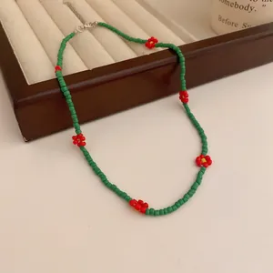 Detailansicht einer handgefertigten grünen Perlenkette mit roten Blumenakzenten