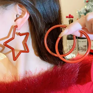 Close-up of stylish red star and hoop earrings worn by a model for a festive look.