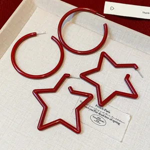Close-up of vibrant red star and hoop earrings on a textured beige background
