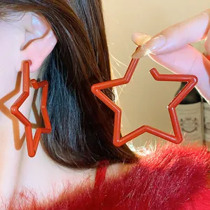 Detail view of bold red star-shaped hoop earrings worn and held against a warm background
