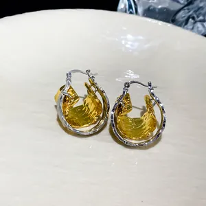 Close-up detail of double-layer hoop earrings with crinkled gold and silver finish