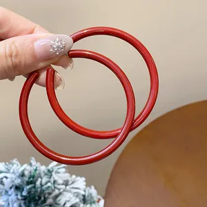 Detailed view of glossy Ankara red hoop earrings being held for size perspective