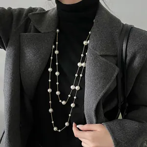 Elegante collana di perle lunga a doppio strato indossata come collana su un cappotto grigio.