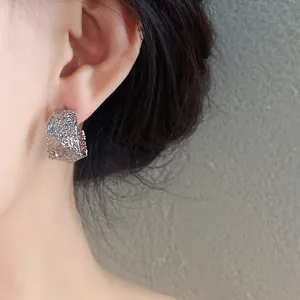 Primer plano de pendientes geométricos en forma de C plateados con textura arrugada