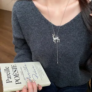 Elegante dettaglio di una collana lunga con ciondolo a cervo e strass su maglione grigio
