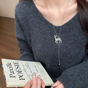 Dettaglio collana con ciondolo cervo e strass su maglione grigio scollo a V chic.