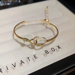 Close-up of gold heart bangle with pavé-set zircons and adjustable infinity chain link