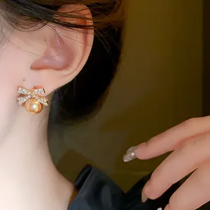 Close-up of elegant bow-knot earrings with gold pearl and sparkling rhinestones on ear.