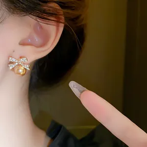 Detailed close-up of a sparkling crystal bow earring with a golden pearl on an ear
