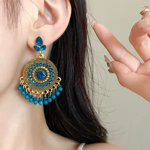Close-up of ornate ethnic style gold earrings featuring blue rhinestones and bead tassels
