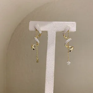 Detailed view of gold spiral earrings with pavé crystals and dangling star charm.