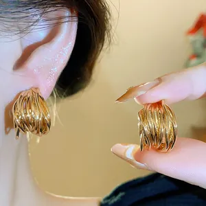 Close-up of elegant gold intertwined wire stud earrings worn on ear and held in hand.