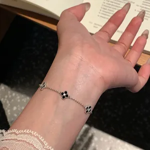 Close-up of a silver four-leaf clover bracelet with black stones on an Asian wrist.