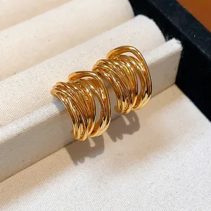 Detailed view of gold-plated multi-layer winding earrings on a cream jewelry tray.