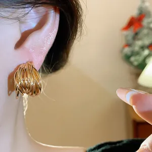 Macro view of gold intertwined stud earrings on ear showing intricate layered metal texture