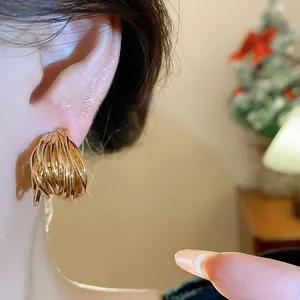 Detailed close-up of gold-plated intertwined stud earrings worn on a female model's ear.