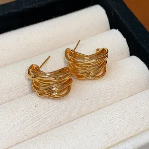 Close-up of elegant gold-plated intertwined earrings on a cream jewelry box insert