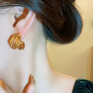 Close-up detail showing elegant gold-plated multi-layer twisted hoop earrings on model's ear.