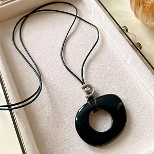 Detailed view of a sleek black resin hollow circular pendant on a long leather cord