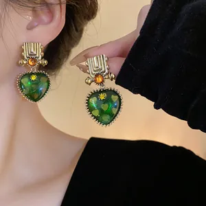 Close-up detail of vintage style green heart earrings with golden geometric top on a model