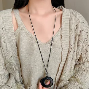 Detail view of a resin hollow round pendant on a black leather cord sweater chain.