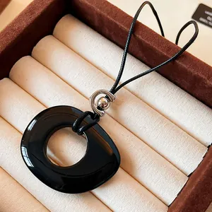 Detailed macro view of a glossy black asymmetric resin pendant on a leather cord.
