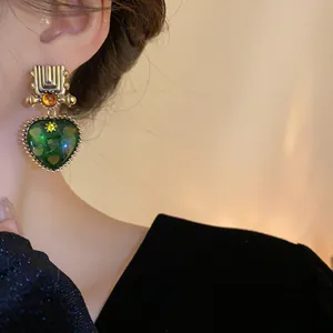 Close-up detail of vintage style geometric earrings with a large green heart pendant
