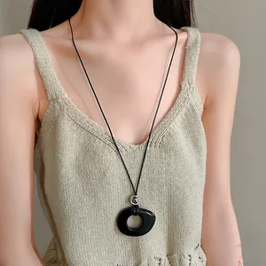 Detail of a minimalist black resin hollow circular pendant on a black cord necklace.