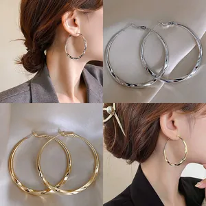 Collage of oversized twisted hoop earrings in gold and silver finishes on a model.