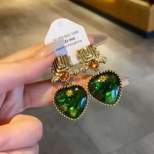 Close-up of vintage heart-shaped earrings with green stones and gold bead trim details