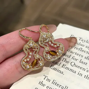 Close-up of hollow gourd earrings with pearls and tiger's eye stone on book background