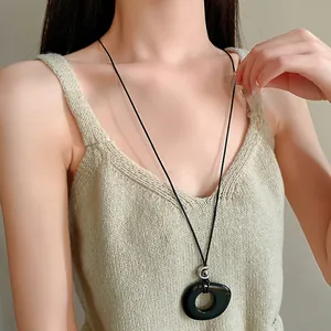 Close-up detail of a minimalist black resin hollow round pendant on a long cord necklace