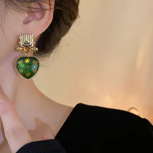 Close-up detail of vintage heart earrings featuring green resin drops and gold accents