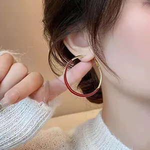 Detailed close-up of a large gold-tone hoop earring with vibrant red enamel detail