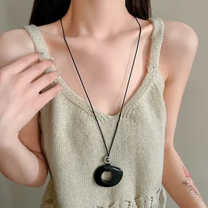 Close-up of a minimalist black resin hollow circular pendant on a black cord necklace