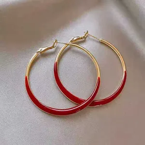Close-up of gold hoop earrings with vibrant red enamel inlay on champagne silk background