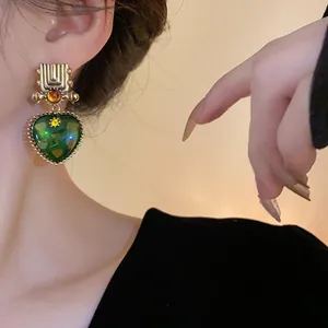 Detail view of vintage heart-shaped green earrings with golden geometric accents on model.