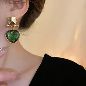 Detail shot of vintage green heart earrings worn on ear, showing light luxury design.