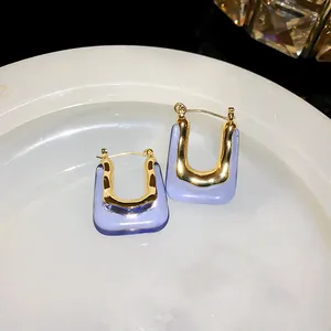 Close-up detail of vintage gold and purple resin U-shaped earrings on a white textured plate