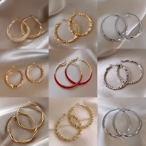 Variety of metallic hoop earrings in gold and silver finishes on neutral silk fabric background