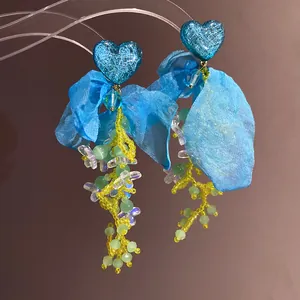 Dettaglio di orecchini a cuore con fiori di chiffon blu e nappe di perline colorate.